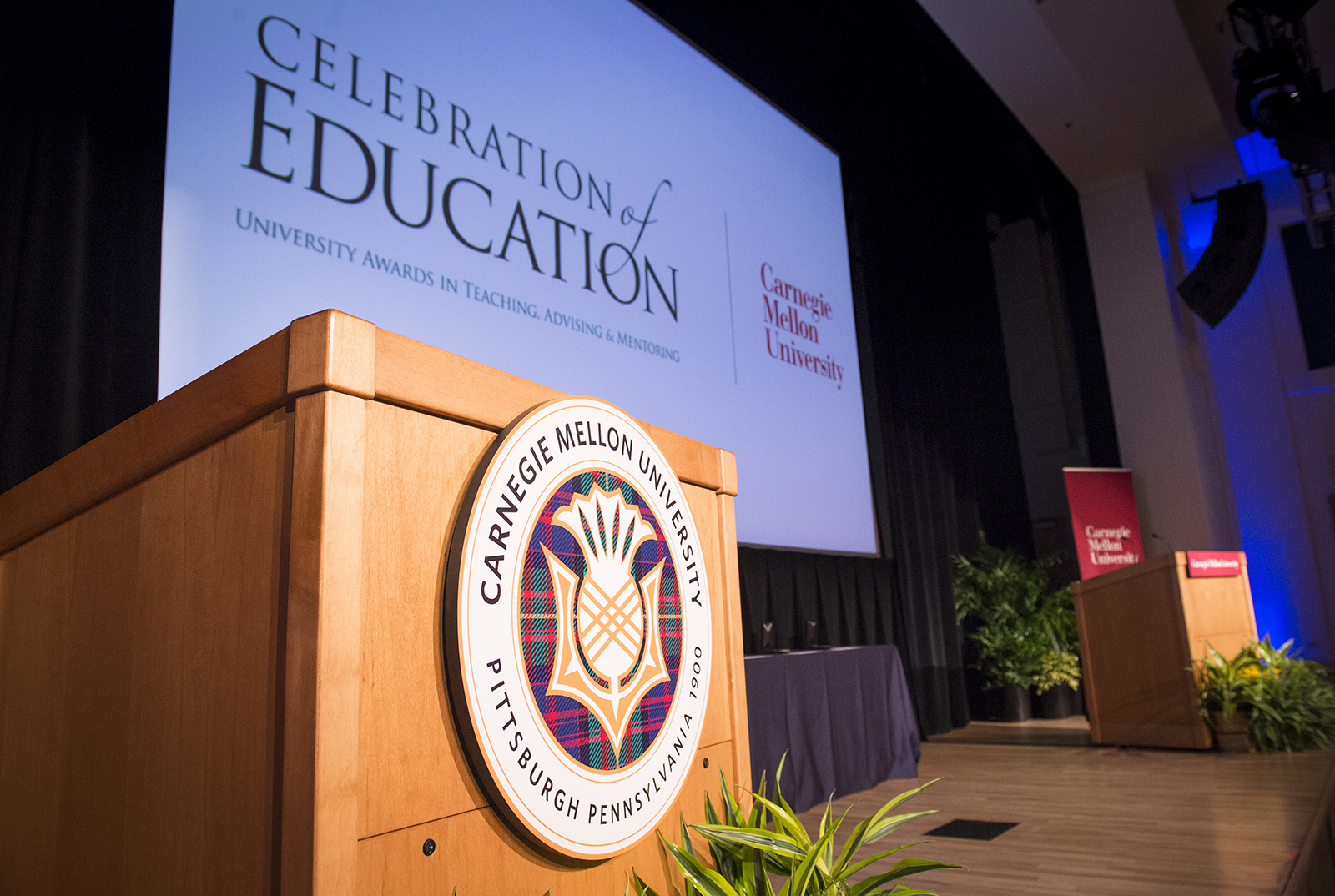 The stage during a previous Celebration of Education. A wooden podium with CMU logo is in the foreground, projector screen in the background