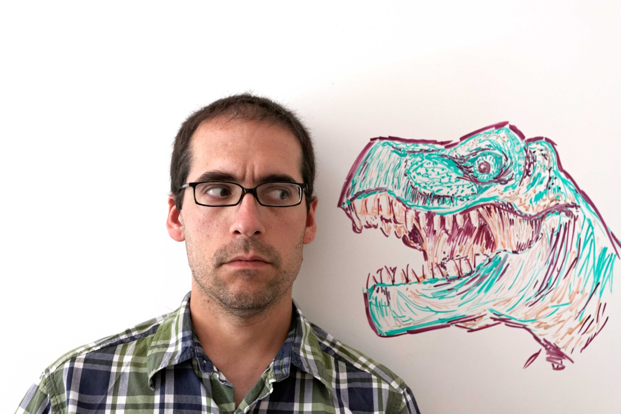 Derek Wahila looks out of the corner of his eye at a dinosaur drawn beside him on a whiteboard
