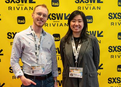 A man and woman stand in front of a yellow backdrop peppered with the SXSW logo.