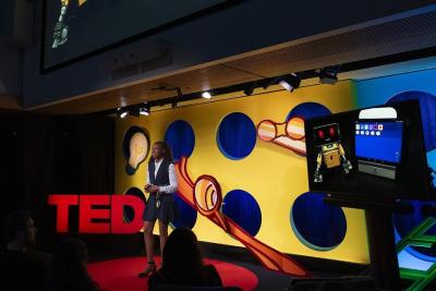 Randi Williams stands on a stage beside large red TED letters, a screen nearby displays a robot 