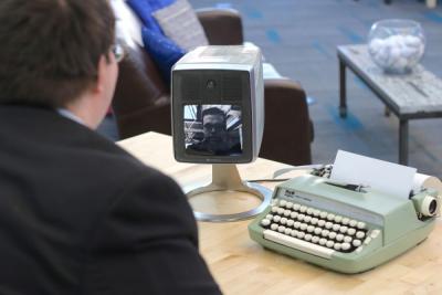 over McGee's shoulder, picturephone and typewriter on table. Harrison speaks via picturephone