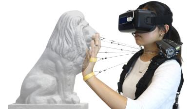 student wearing VR headset on face touches the face of a lion statue while wires connect fingers to the Wireality device on her shoulder