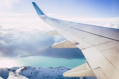 looking of the left side of a plane in flight, view of the left wing flying over snowcapped mountains