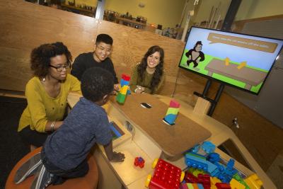 3 adults and a child sit at the NoRILLA table and build towers with blocks