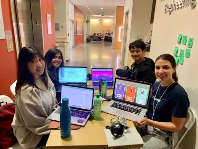 4 students at a table during the hackathon & show their laptop screens while working on Lucid Drums