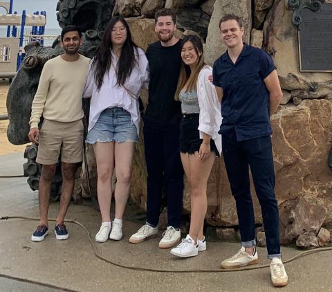 5 students of team CarMax stand by a giant Neptune statue at the beach