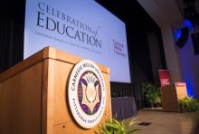 The stage during a previous Celebration of Education. A wooden podium with CMU logo is in the foreground, projector screen in the background