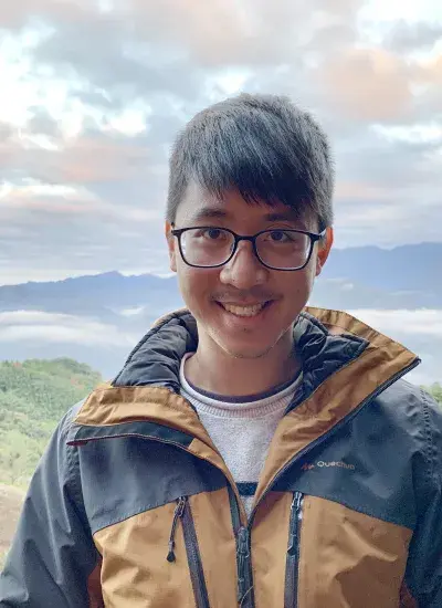 Photo of PhD student Hank Lee with grass and mountains in background