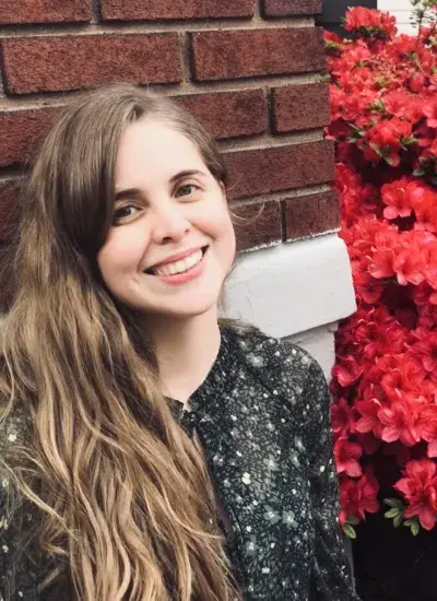 Photo of PhD student Stephanie Valencia in front of brick wall with foliage to right