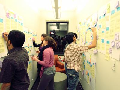 five students diagramming with colorful note paper on both walls of a narrow hallway 