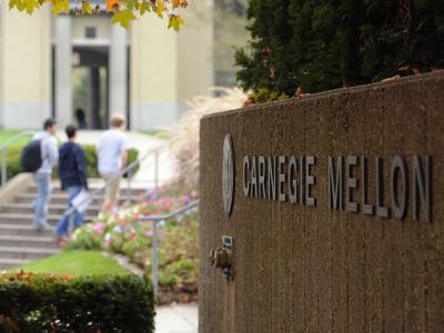 Carnegie Mellon University stone sign in the foreground, people walking up steps in the background