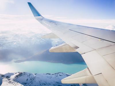 looking of the left side of a plane in flight, view of the left wing flying over snowcapped mountains