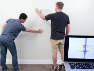 Wall++ technology developed by Carnegie Mellon University and Disney Research can turn an entire wall into a touchpad. It also serves a sensor for electromagnetic activity. Two men stand in front of a white wall. The locations of where they are touching the wall are visible on a nearby laptop screen.