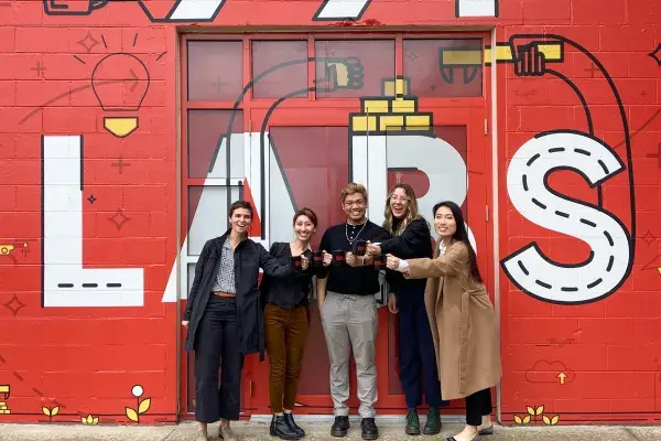 5 team members stand in front of a red wall with 99P Labs painted in white