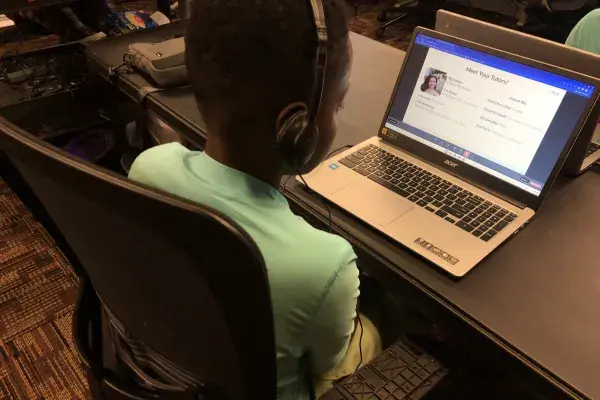 A middle school student is seated at a laptop during introductions to their tutor, a university student.