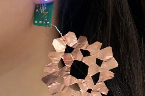 A close-up shot of an earring in human's ear, attached to a circuit board.