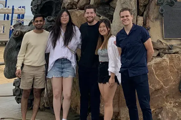 5 students of team CarMax stand by a giant Neptune statue at the beach