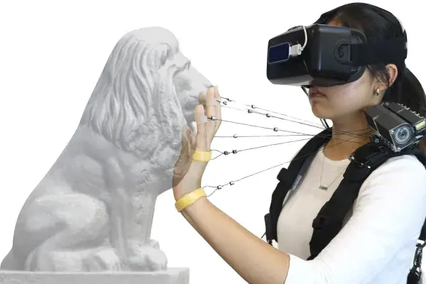 student wearing VR headset on face touches the face of a lion statue while wires connect fingers to the Wireality device on her shoulder